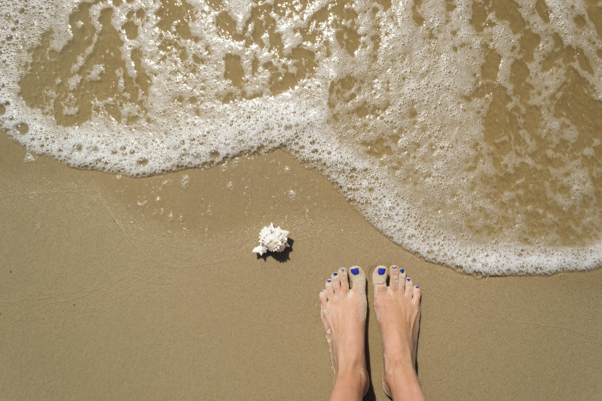 feet in sand with ocean waves coming in to represent best beach vacations in the us